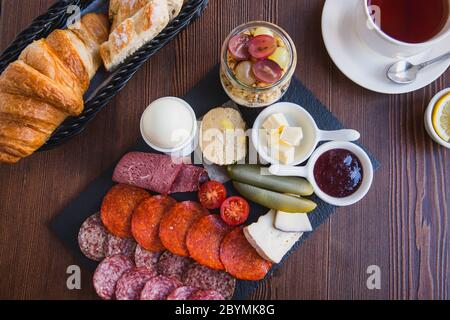 Brunch oder Frühstück, verschiedene Gerichte mit Ei, Salami, Fleisch- und Käsesorten, Müsli, Smoothie, Obst und Beeren. Serviert mit Brot und einem c Stockfoto