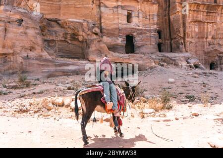 Ein junges Mädchen, das auf einem Esel durch die breiten Straßen einer alten Stadt Petra, Jordanien, reitet. Eines der sieben Weltwunder. Stockfoto