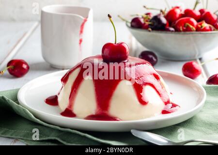 Italienisches Panna Cotta Dessert mit Kirschcoulis auf einem weißen Holztisch Stockfoto
