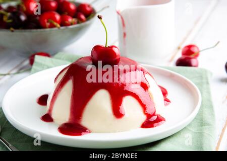 Italienisches Panna Cotta Dessert mit Kirschcoulis auf einem weißen Holztisch Stockfoto