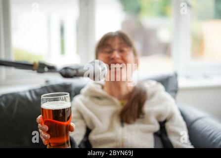Isolierte junge Frau, die zu Hause Bier trinkt und ins Mikrofon singt. Betrunkene Frau, die ein Bier hält und sich amüsiert! Trinken von überschüssigem Alkohol. Stockfoto
