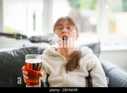 Isolierte junge Frau, die zu Hause Bier trinkt und ins Mikrofon singt. Betrunkene Frau, die ein Bier hält und sich amüsiert! Trinken von überschüssigem Alkohol. Stockfoto