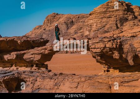 Stilvolle Mädchen in stehen durch den Blick aus einem Panoramablick auf natürliche Felsbrücke und Wadi Rum Wüste, Jordanien Stockfoto