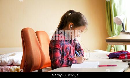 Porträt von glücklichen lächelnden Mädchen, das Musik hört, während Schulaufgaben im Schlafzimmer machen Stockfoto