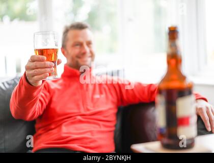 Prost! Nahaufnahme eines isolierten lächelnden Mannes, der zu Hause Bier trinkt und ein Pint genießt. Menschen, die Alkohol zu Hause während der britischen Lockdown Pubs geschlossen. Stockfoto