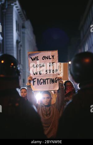 Junge Studentin mit Plakat und Protest. Gruppe von Demonstranten, die vor Polizeikräften protestieren. Stockfoto