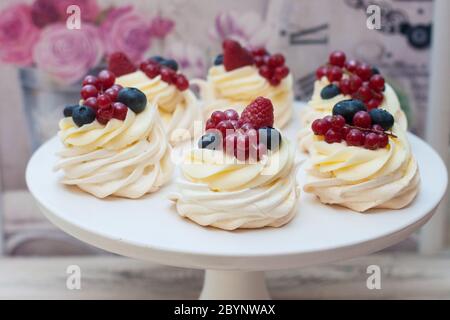 Sechs Mini Pavlova-Baiser-Kuchen mit Schlagsahne, frischer roter Johannisbeere, Himbeere und Heidelbeere auf weißem Cakestand. Stockfoto