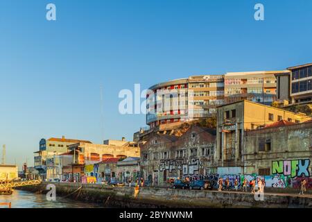 Menschen, die bei Sonnenuntergang in Almada an alten, verlassenen und mit Graffiti bedeckten Fabriken vorbei gehen. Stockfoto