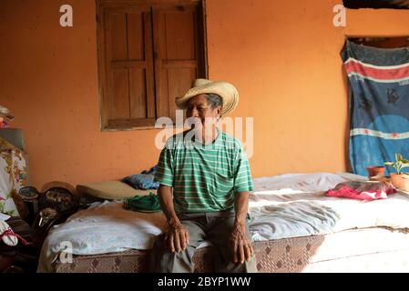 Portrait des Latino-Mannes, der nach der Siesta auf dem Bett sitzt (Mittagsschlaf). Alltag in El Paredón, Guatemala. Dezember 2018 Stockfoto