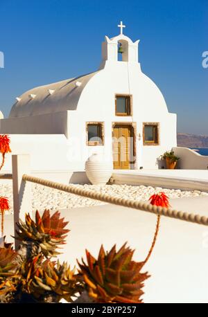 Kleine weiße Kirche mit weißem Vorplatz im Dorf Oia in Santorini, Griechenland, mit Blick auf die Ägäis. Stockfoto