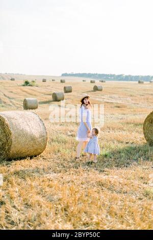 Sommer helle Porträt von kleinen Mädchen spielen mit ihrer Mutter, trägt ähnliche gestreifte Kleider, in schönen Feld mit Heuballen auf dem Hintergrund Stockfoto