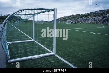 Linien um das Fußballfeld, Eckseite, aus Kunstrasen. Blick hinter das Netz auf den Fußballplatz auf den Lofoten Inseln, umgeben von Felsen Stockfoto