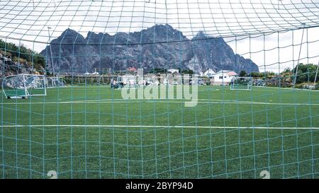 Linien um das Fußballfeld, Eckseite, aus Kunstrasen. Blick hinter das Netz auf den Fußballplatz auf den Lofoten Inseln, umgeben von Felsen Stockfoto