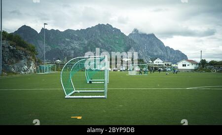 Linien um das Fußballfeld, Eckseite, aus Kunstrasen. Blick hinter das Netz auf den Fußballplatz auf den Lofoten Inseln, umgeben von Felsen Stockfoto