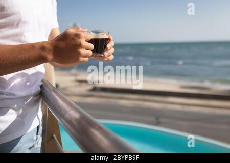 Mittlere Ansicht eines kaukasischen Mannes, der auf einem Balkon steht und eine Tasse Kaffee hält Stockfoto