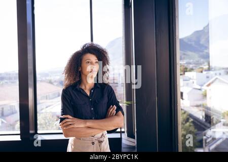 Junge Mischrennbusinessfrau, die vor den Fenstern steht Stockfoto
