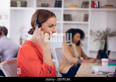Junge glückliche kaukasische Geschäftsfrau, die mit Headset arbeitet Stockfoto