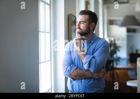 Kaukasischer Mann, der neben einem Fenster in einem Büro denkt Stockfoto