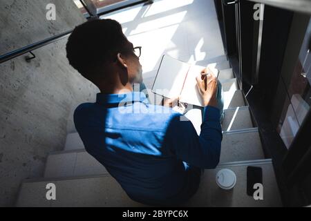 Afroamerikanischer Mann sitzt auf Treppen und schreibt in einem Notizbuch Stockfoto