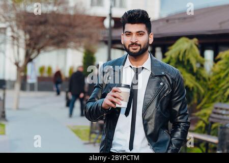 Stilvoller bärtiger Indianer, der auf der Straße Kaffee zum Mitnehmen trinkt. Stockfoto