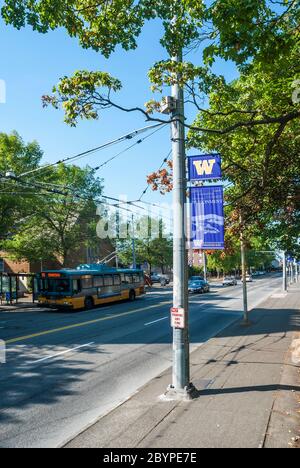 Banner der Universität von Washington auf einer Straße im Universitätsviertel im Bundesstaat Washington. Im Bild ist ein elektrischer Bus für den öffentlichen Nahverkehr. Stockfoto