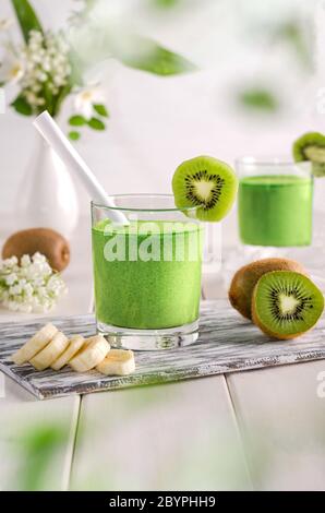 Obst-Smoothie mit Kiwi und Banane auf einem weißen Holztisch in einer Glastasse. Stockfoto