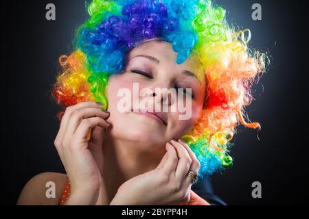 Frau in Clowns Perücke lächelnd ziehen gefälschte Haare an den Seiten Stockfoto