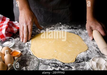 Herrenhände bereiten Teig für Pizza auf einem schwarzen Tisch zu Stockfoto