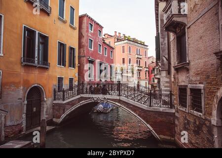 Zwei Liebhaber sitzen Seite an Seite auf einer Brücke über einen Kanal zwischen rosa und gelben alten Gebäuden in Venedig, Italien Stockfoto