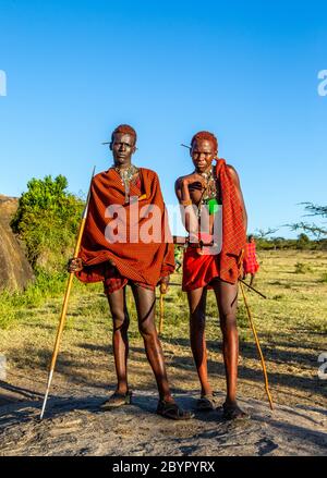 Zwei junge Masai-Krieger in traditioneller Kleidung und Waffen stehen in der Savanne. Tansania, Ostafrika, 12. August 2018. Stockfoto