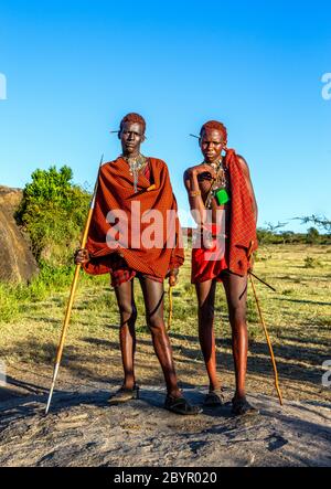 Zwei junge Masai-Krieger in traditioneller Kleidung und Waffen stehen in der Savanne. Tansania, Ostafrika, 12. August 2018. Stockfoto