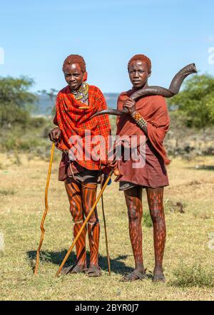 Zwei junge Masai-Krieger in traditioneller Kleidung und Waffen stehen in der Savanne. Tansania, Ostafrika, 12. August 2018. Stockfoto