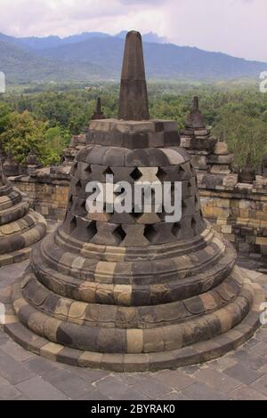 Eine Stupa im Vordergrund und Stupas im Hintergrund auf dem Candi Borobudur, dem größten buddhistischen Tempel der Welt. Berge und Wolken bei Sonnenuntergang, Stockfoto