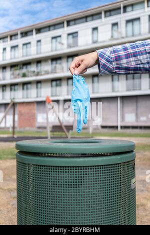 Weibliche Hand wirft Schutzhandschuh in den Mülleimer eines Parks. Coronavirus oder Covid-19 Abfallkonzept Stockfoto