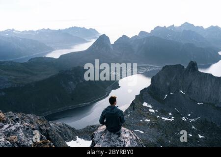 Männlicher Wanderer feiert Erfolg auf einem Berg und blickt auf ein Tal. Reisen Sie Mann allein auf der Kante Klippe in den Bergen über Fjord Wandern Stockfoto