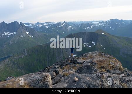 Ein Wanderer hoch oben mit Panoramablick auf Henningsvaer Küste und Inselchen. Steht und genießt Blick auf das Tal von hügeligen Aussichtspunkt. Wanderer hat oben erreicht Stockfoto