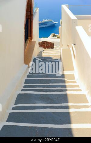 Treppen führen den Rand der Caldera hinunter durch das weiß gestrichene Dorf auf der griechischen Insel Santorini mit Blick auf ein Kreuzfahrtschiff auf der Ägäis Stockfoto