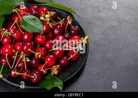 In der Nähe von Pile von reifen Kirschen mit Stengel und Blätter. Große Sammlung von frischen roten Kirschen. Reifen Kirschen Hintergrund Stockfoto