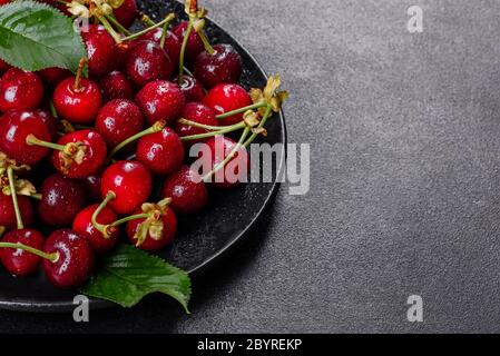 In der Nähe von Pile von reifen Kirschen mit Stengel und Blätter. Große Sammlung von frischen roten Kirschen. Reifen Kirschen Hintergrund Stockfoto