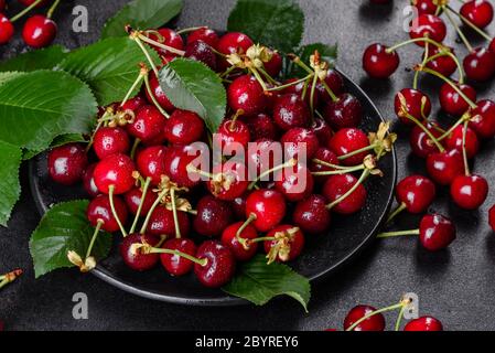 In der Nähe von Pile von reifen Kirschen mit Stengel und Blätter. Große Sammlung von frischen roten Kirschen. Reifen Kirschen Hintergrund Stockfoto