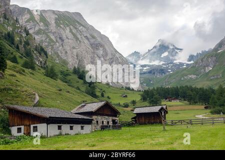 Grünes majestätisches Tal mit Tiroler Häusern auf dem Hintergrund von alpinen Gipfeln im Nebel. Wanderreise Outdoor-Konzept, Reise in die Berge, Kals A Stockfoto