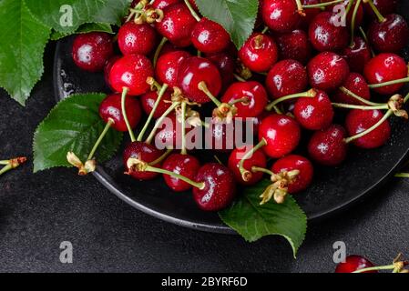 In der Nähe von Pile von reifen Kirschen mit Stengel und Blätter. Große Sammlung von frischen roten Kirschen. Reifen Kirschen Hintergrund Stockfoto