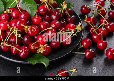 In der Nähe von Pile von reifen Kirschen mit Stengel und Blätter. Große Sammlung von frischen roten Kirschen. Reifen Kirschen Hintergrund Stockfoto