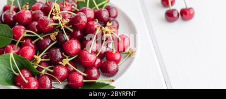 In der Nähe von Pile von reifen Kirschen mit Stengel und Blätter. Große Sammlung von frischen roten Kirschen. Reifen Kirschen Hintergrund Stockfoto