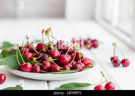 In der Nähe von Pile von reifen Kirschen mit Stengel und Blätter. Große Sammlung von frischen roten Kirschen. Reifen Kirschen Hintergrund Stockfoto