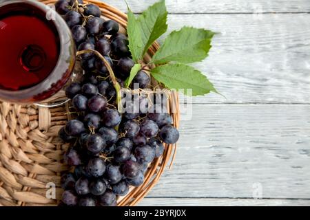 Eine Gruppe von dunklen Trauben und Weinglas auf einem runden Strohhalmtablett und grauen Holztisch und Kopie Raum Stockfoto