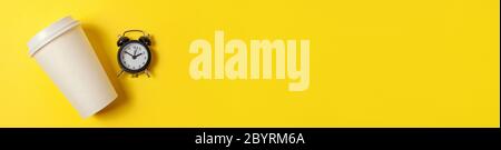Einfach minimalistisches Design Papier Kaffeetasse und Wecker auf gelb bunten Hintergrund. Getränke zum Mitnehmen und Frühstücksgetränk. Good Morning Wake Up Wake-Konzept. Flach Lay Draufsicht Copy Space Banner Stockfoto