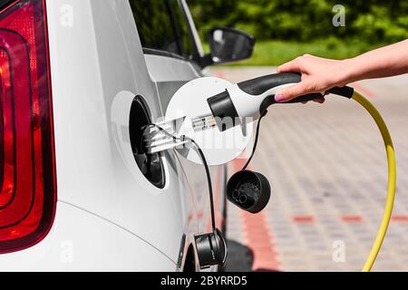 Nahaufnahme Frau Hände stecken ein Netzkabel zu Elektroauto zum Laden an der Ladestation im Freien. Stockfoto