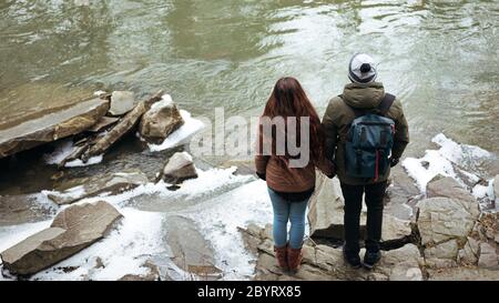 Junge Reisende, die auf Felsen am Fluss stehen und die Hände halten Stockfoto