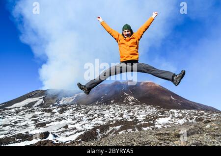 Ein Mann in orangefarbener Jacke sprang einen Tag vor dem Ausbruch auf dem Ätna, Sizilien, Italien, mit den Dämpfen des Vulkans Stockfoto